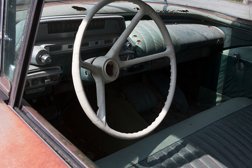 Interior of rotten old American car with white steering wheel and broken armature board