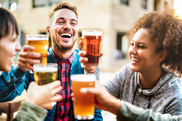 multicultural happy friends drinking and toasting beer at brewery bar restaurant - beverage life style concept with men and women having fun together out side - bright warm filter with focus on guy - beer pub women pint glass imagens e fotografias de stock