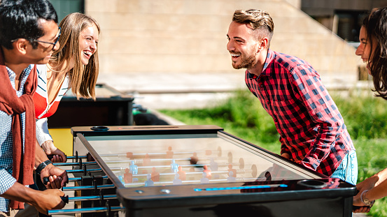 Multicultural friends play kicker table foosball at open space bar -Friendship life style concept with happy millennial having fun together at garden party - Bright warm filter with focus on right guy