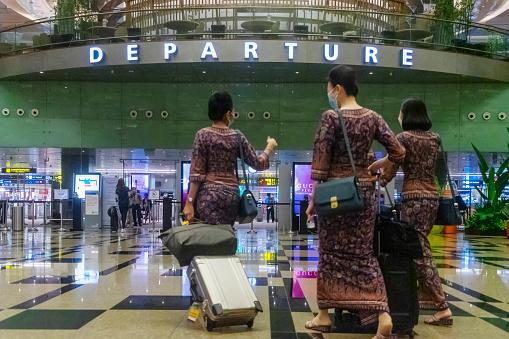 Singapore, Singapore - November 1, 2021: Flight stewardesses with Singapore Airlines, clad in their traditional sarong kebaya uniforms, walk towards the departure gate at Terminal 3, Changi Airport.