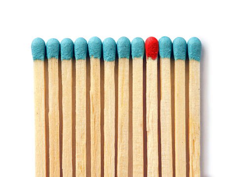 Light blue group of matchsticks in a row with one in red isolated on white background. Standing out from the crowd/leadership concept.
