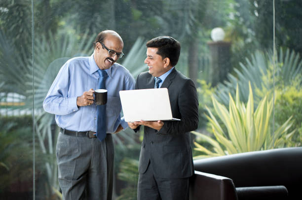 istock Two businessmen laughing while drinking coffee and using laptop at office 1350664478