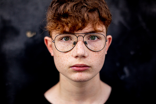 close-up  of red-haired teenage boy with freckles, against a black wall in the street