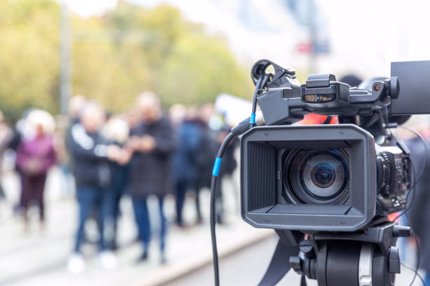 istock Video camera lens in the focus, blurred people in the background 1350664991