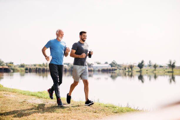 feliz padre e hijo atléticos corriendo mientras hacen ejercicio juntos en la naturaleza. - family sport exercising jogging fotografías e imágenes de stock
