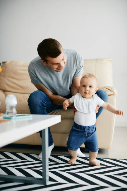 istock Cute little boy taking his first steps with help of a father at home. 1350671429