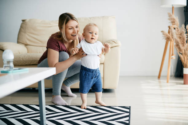 istock Happy mother assisting her small son in taking first steps at home. 1350671455