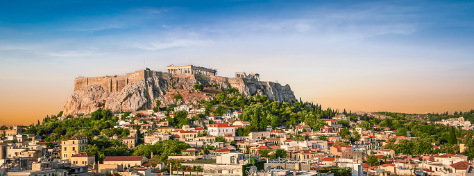 Acropolis site with Parthenon on the hill at the city of Athens, Greece. Blue and orange sky at sunset. Popular travel destination in Europe. Bright and wide image.