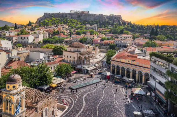 Aerial view of popular Monastiraki square with the church of Pantanassa and the city view with the Acropolis site and Parthenon on the hill on a beautiful day with fascinating sky during sunset. Popular travel destination in Europe.