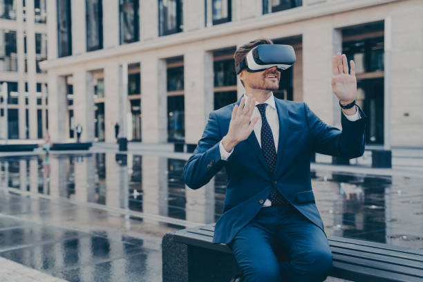istock Man in VR goggles trying to reach something in virtual reality with his hands while sitting outdoors 1350674642
