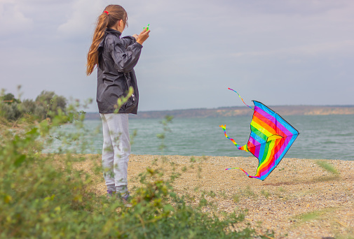 Teenage girl playing with a bright colorful kite on the shore of a pond. concept of outdoor activities and a healthy lifestyle.