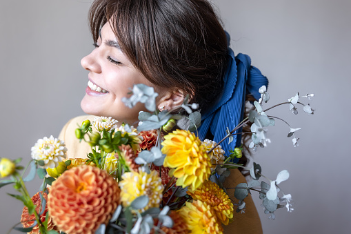 Young woman with a blue ribbon in her hair, holding a bouquet of yellow and orange chrysanthemums, gray background.