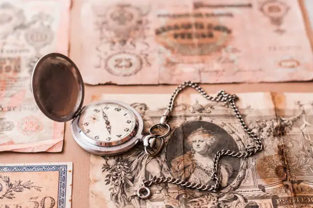 Photo of Old worn out of circulation ruble banknotes of tsarist russia and a watch on a chain on a brown background