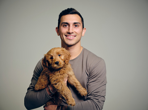 A headshot portrait of a man holding a Golden Doodle puppy dog.