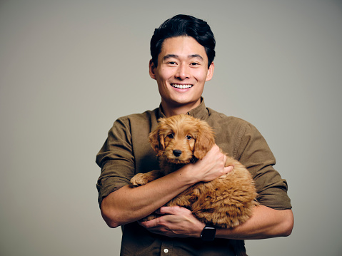 A headshot portrait of an Asian Korean man holding a Golden Doodle puppy dog.