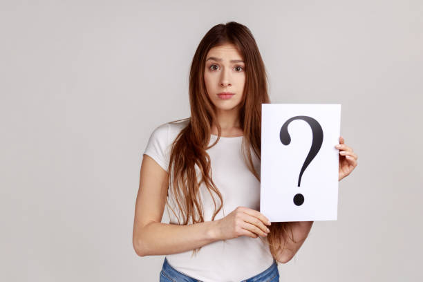 istock Confused thoughtful woman looking at camera, holding paper with question mark, thinks about tasks. 1350691462