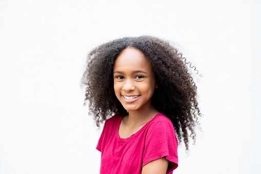 Black girl smiling and looking at camera, with black power hair. White background.