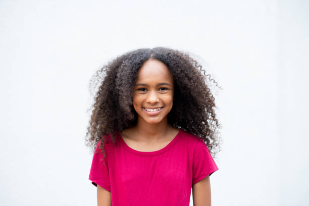 Black girl smiling and looking at camera, with black power hair. White background.