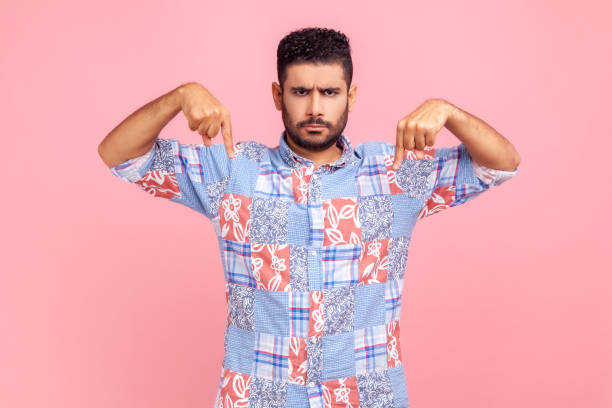 istock Here and now! Strict bearded handsome man pointing finger down, looking at camera with serious bossy facial expression, wearing blue casual shirt. 1350692503