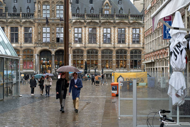 Ghent, Belgium - October 30, 2021: People walk outdoors on a rainy day in Ghent, in the background a tram runs on its line.