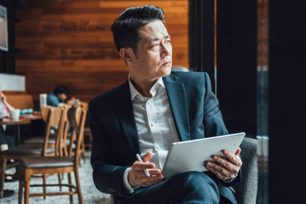 istock Handsome Asian Businessman Using Digital Tablet in a Cafe 1350699860