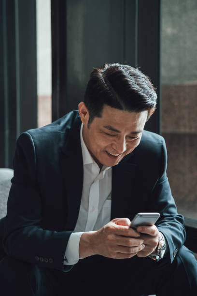 istock Happy Asian Businessman Using Mobile Phone in a Cafe 1350699888