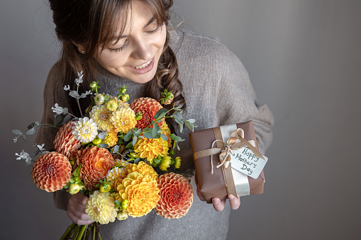 Attractive young woman with a mother's day gift and a bouquet of chrysanthemum flowers in her hands.
