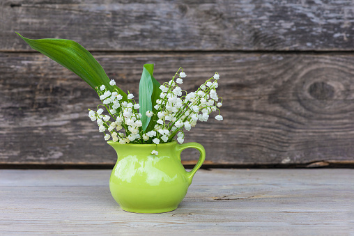 Bouquet of lilies of the valley in green jug on rustic wooden background,