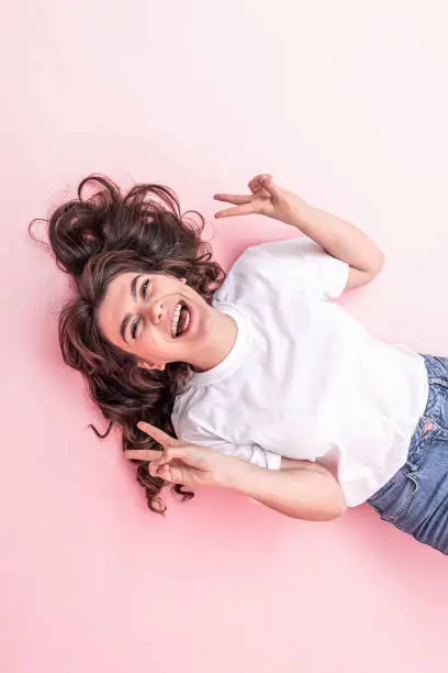 Attractive brunette girl in a white T-shirt smiles on a pink background.