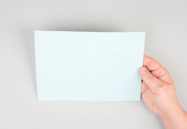 istock Woman holds a blank sheet of paper, grey colored background, empty copy space for text, minimalism 1350710592