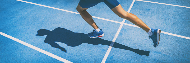 Sprinting man runner sprinter athlete running shoes and legs on track and field lane run race competing fast panoramic banner background.