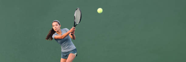 giocatore di tennis che gioca sullo striscione del cemento all'aperto. atleta donna asiatica che colpisce la palla con la racchetta durante il colpo di testa panoramico della partita. su banner verde. sport in competizione. - tennis court tennis racket forehand foto e immagini stock