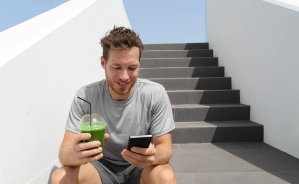 zielony sok z smoothie pije człowiek pijący detoksykacyjny koktajl białkowy za pomocą aplikacji na telefon komórkowy do śledzenia żywieniowego planu posiłków dietetycznych. zdrowy styl życia. - cold pressed zdjęcia i obrazy z banku zdjęć