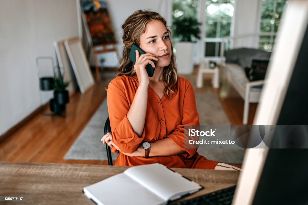 Young woman talking on smart phone at home office Young woman talking on smart phone while working at home office Using Phone Stock Photo