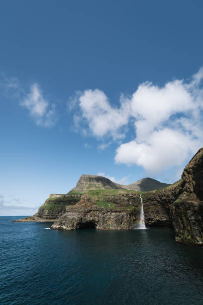 Mulafossur waterfall that drops into the ocean in Gasadalur on Faroe Islands Beautiful Mulafossur waterfall that drops into the ocean in Gasadalur on Faroe Islands. Sunny day with beautiful clouds and blue sky vágar photos stock pictures, royalty-free photos & images