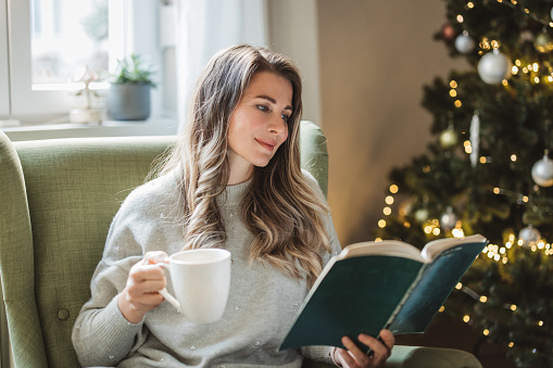 Mature woman reading book for Christmas at home. She is enjoying in her time.