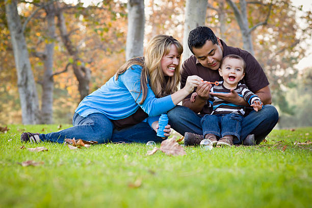 famille ethnique de race mixte heureux jouant avec des bulles dans le parc - bubble wand outdoors little boys mother photos et images de collection