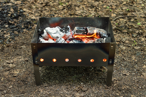 Small lightweight portable barbecue grill for camping with burning coals. Before barbecuing.