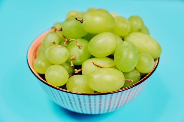 Green table grapes on bowl on blue background. Healthy diet