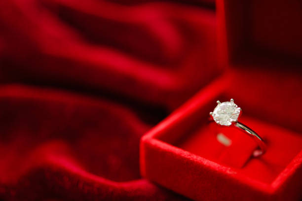 istock Diamond ring in jewelry gift box on red fabric background 1350730455