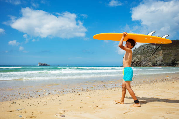 istock Boy walk into the sea holding surfboard over head 1350731746