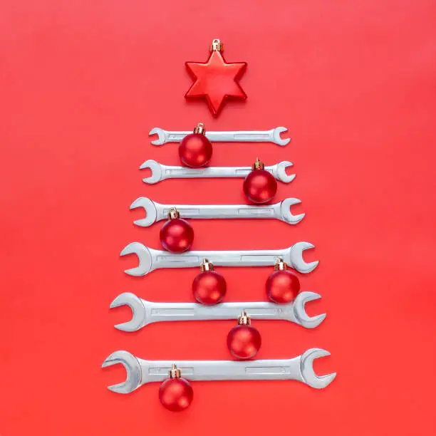 Photo of Creative christmas tree on red background, made of wrenches. Industrial greeting card and happy new year concept. Square