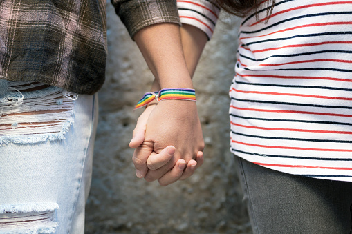 Close up of happy lesbian couple holding hands wearing rainbow flag wristband, LGBT love concept. High quality photo
