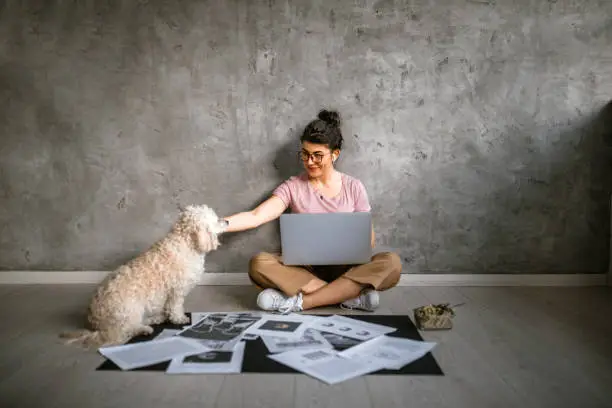 Photo of Young creative woman working sitting on floor in company of her cute dog