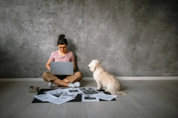 Photo of Young creative woman working sitting on floor in company of her cute dog