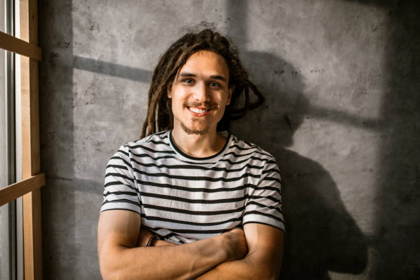 istock Man with dreadlocks leaning gray concrete wall next to the window in modern office 1350739299