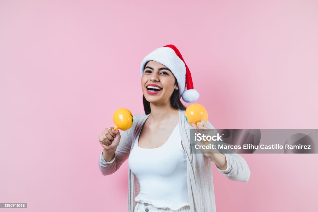 Portrait of young latin woman holding maracas rattle with copy space in a christmas concept on pink background Maraca Stock Photo