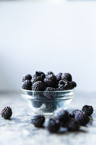 Ripe blackberry on a table. Wild black raspberries in glass bowl on light background. Fresh berry