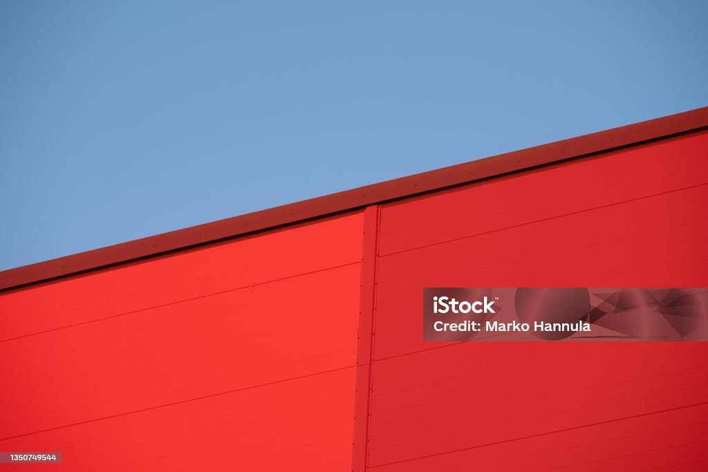 Closeup of red metallic building wall against bright blue sky during the sunset. Helsinki / Finland - NOVEMBER 1, 2021: Closeup of red metallic building wall against bright blue sky during the sunset. Architecture Stock Photo