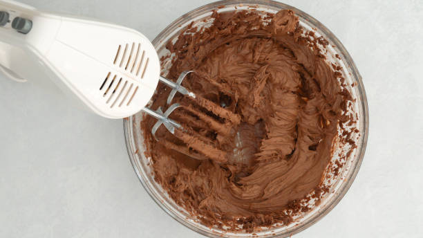 glaçage au chocolat dans un bol en verre, mélange des ingrédients ensemble à l’aide d’un mélangeur électrique - crème au beurre photos et images de collection